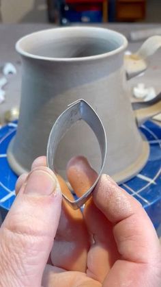 a person holding a ring in front of a cup on top of a blue table