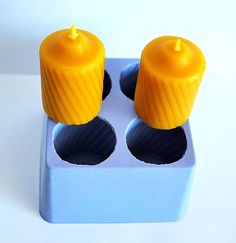 two yellow candles sitting on top of a blue box with holes in it's sides