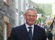 a man in a suit and tie standing on the street with people walking down it