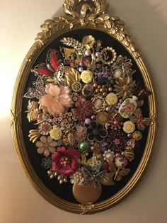 an ornate gold frame with flowers and other things on it is hanging on the wall