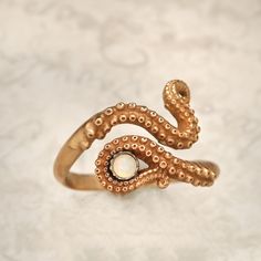 an octopus ring with a pearl in it's mouth on a white surface,