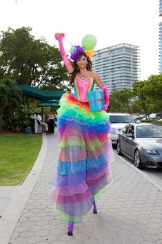 a woman in a multicolored dress is walking down the street with balloons on her head