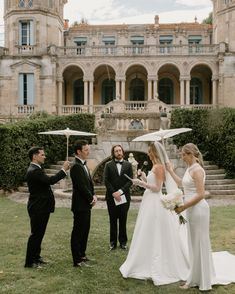 a bride and groom standing under an umbrella in front of a mansion with two men