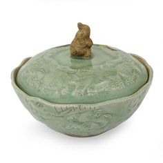 a green ceramic bowl with a small bear on it's top, and a lid in the shape of a bowl