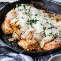 a skillet filled with chicken covered in cheese and onions on top of a table