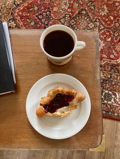 a pastry on a plate next to a cup of coffee with a book and pen