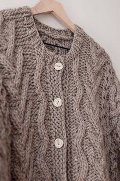 a gray sweater hanging on a wooden hanger next to a white wall with buttons