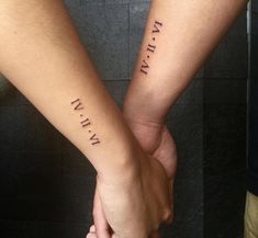 two people holding hands with roman numerals tattooed on their arms and the words written in cursive font