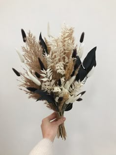 a person holding a bunch of dried flowers in their hand with white and black feathers