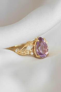 a close up view of a ring with a pink stone in the center on a white cloth