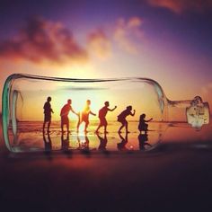 a group of people holding hands in a bottle with the sun setting behind them on the beach