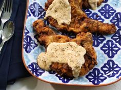 chicken wings covered in gravy on a blue and white plate with silverware