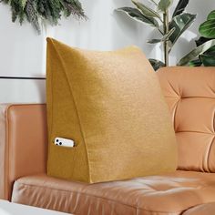 a couch with a pillow and remote control on the arm rest in front of a potted plant