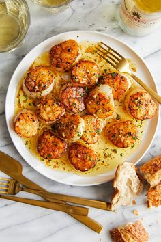 a white plate topped with scallops covered in sauce next to bread and wine glasses