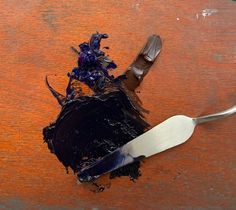 a knife and some black paint on a table with an orange wall in the background