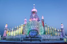 an ice sculpture is lit up with colorful lights and buildings in the background at night