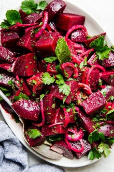 a white plate topped with beets and cilantro next to a silver spoon