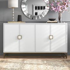 a white dresser with flowers and a round mirror on the wall above it in a living room