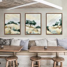 three paintings hang on the wall above a table with four stools in front of it