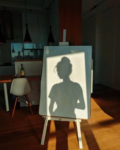 a shadow of a woman is on an easel in the middle of a room