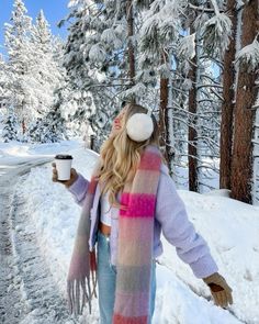 a woman is walking in the snow holding a cup of coffee and wearing a scarf