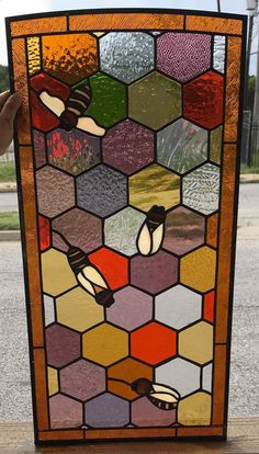 a hand holding up a stained glass window in the shape of a beehive