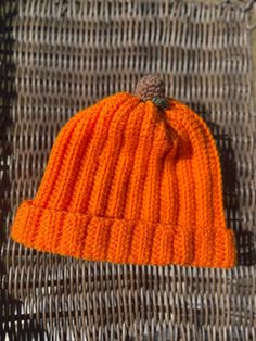 an orange knitted hat sitting on top of a wicker chair