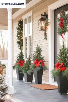 three potted christmas trees on the front porch with red bows and lights hanging from them