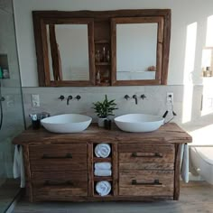 two white bowls are sitting on top of a wooden cabinet in the bathroom, with mirrors above them