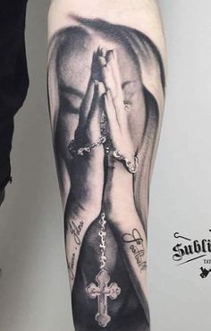 a man's leg with a tattoo on it and hands holding a cross in front of him