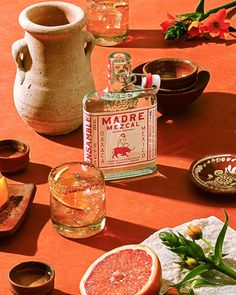 a table topped with bottles and glasses filled with oranges on top of a red surface