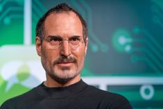 a man wearing glasses and a black t - shirt is standing in front of a green background