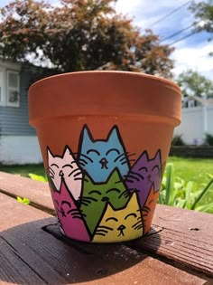 a pot with cats painted on it sitting on a wooden table in front of a house