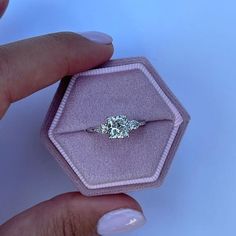 a woman's hand holding an engagement ring in a pink velvet box on a white background