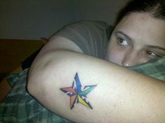 a woman with a colorful star tattoo on her arm, resting comfortably on a bed