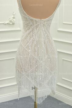 the back of a white dress with beading and fringes on display in a room