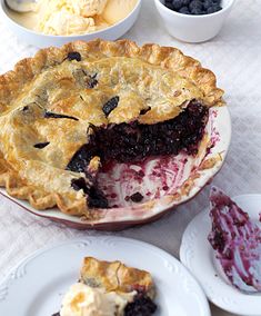 a pie with a slice taken out of it on a white table cloth next to other plates and utensils