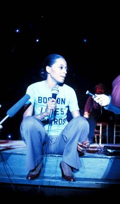 a woman sitting on top of a stage holding a microphone next to a man standing behind her