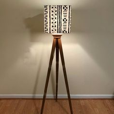 a wooden tripod floor lamp with a black and white patterned shade on the top