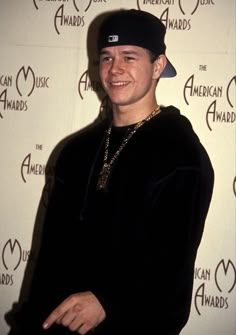 a young man wearing a black hat and smiling at the camera while standing in front of an american music awards backdrop