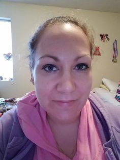 a woman with blue eyes wearing a pink scarf and smiling at the camera while standing in front of a bed