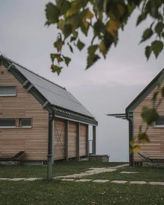 two wooden buildings sitting next to each other on top of a grass covered field near the ocean