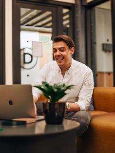 a man sitting in front of a laptop computer on top of a wooden table next to a potted plant