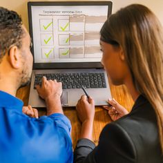 a man and woman sitting at a desk with a laptop on which they are doing tasks