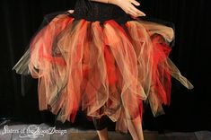 a woman in a black dress with red and orange tulle on her skirt is posing for the camera