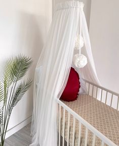 a bed with a white canopy over it next to a potted plant and a red pillow