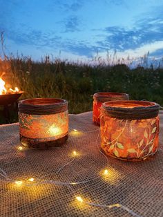 three jars sitting on top of a table next to a campfire with lights around them