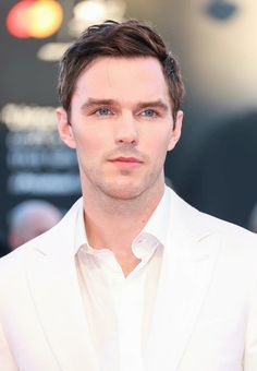 a man in a white suit looks at the camera while standing on a red carpet