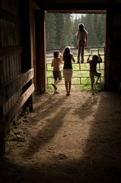 three children are standing in the doorway of a barn looking at an adult on a horse