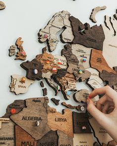 a person's hand is pointing at the map of the world with pins on it